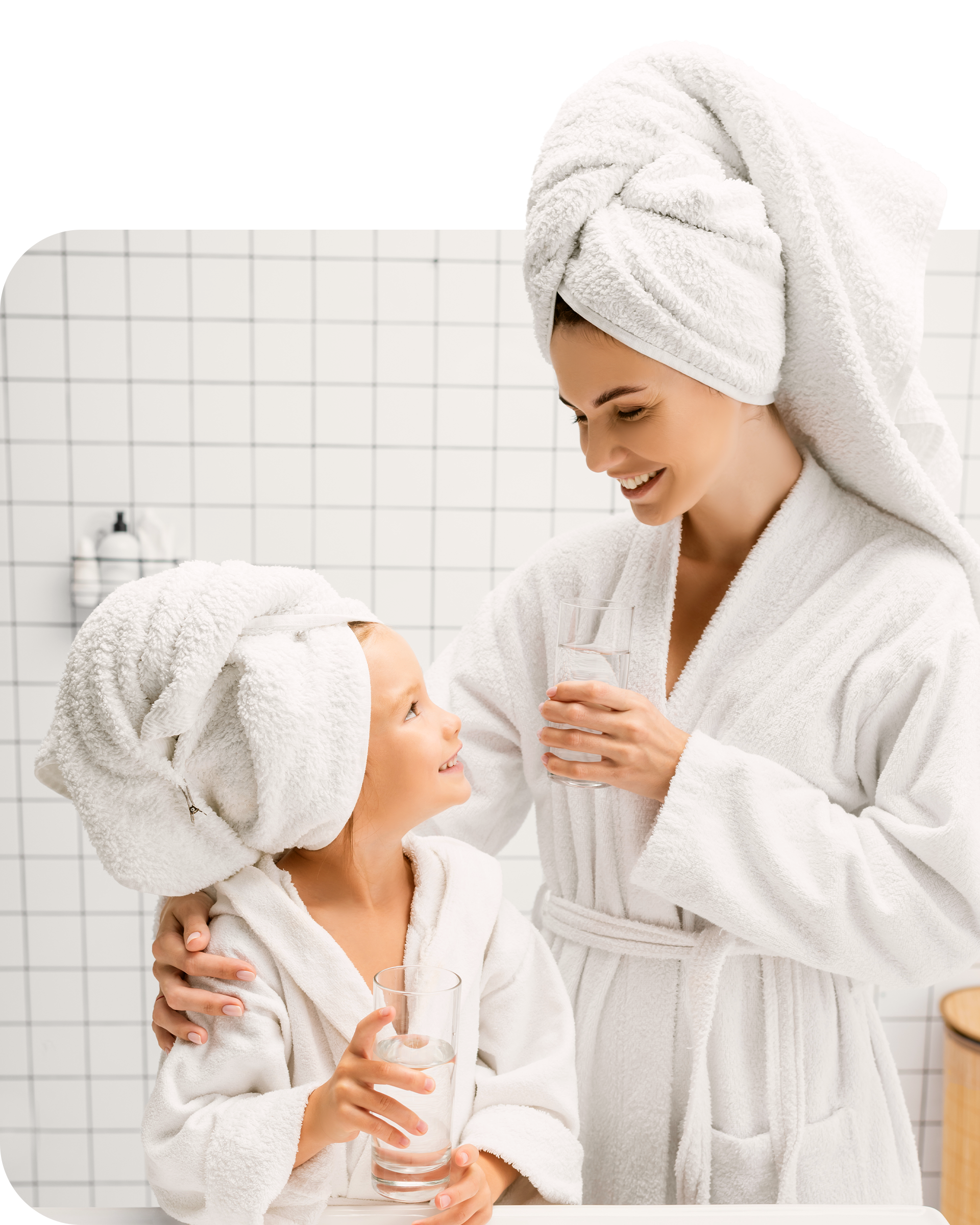 Parent and child in matching white bathrobes smiling at each other.